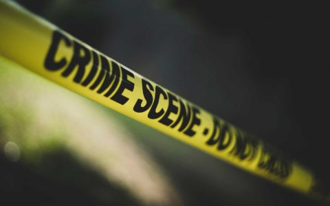 Yellow police tape reading CRIME SCENE DO NOT CROSS stretched across a dark background