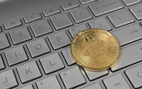 A gold Bitcoin coin resting on a laptop keyboard