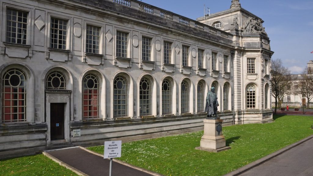 The stone facade of Cardiff Crown Court with arched windows and a lawn