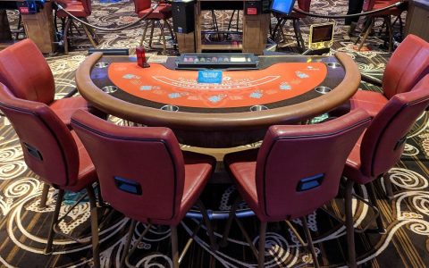 An empty blackjack table with red chairs on a casino floor