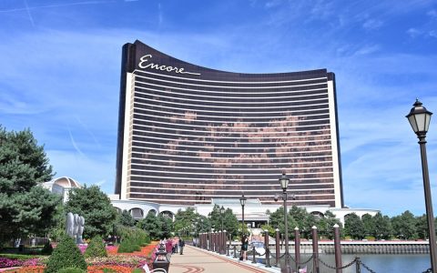 The curved bronze tower of Encore Boston Harbor in Everett seen from a waterfront walkway with flower beds