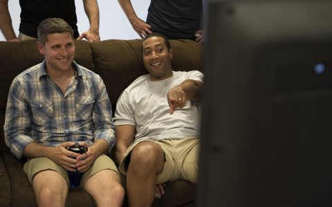 Two adults sit on a couch playing a video game