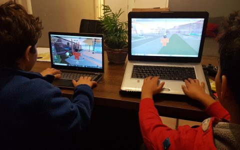 Two children play an online game on laptops