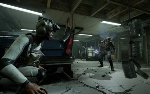 A test subject wearing night-vision goggles crouches behind a car while an enemy searches a dim garage