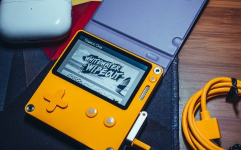 A yellow Playdate handheld on a desk beside an orange USB-C cable