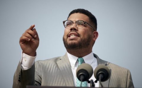 State Rep. Manny Guzman speaking at a podium with microphones