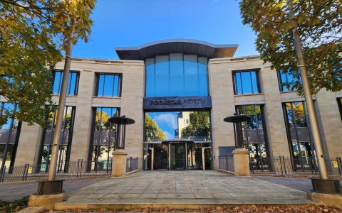 The stone and glass front of the Rockstar North building in Edinburgh, framed by autumn trees