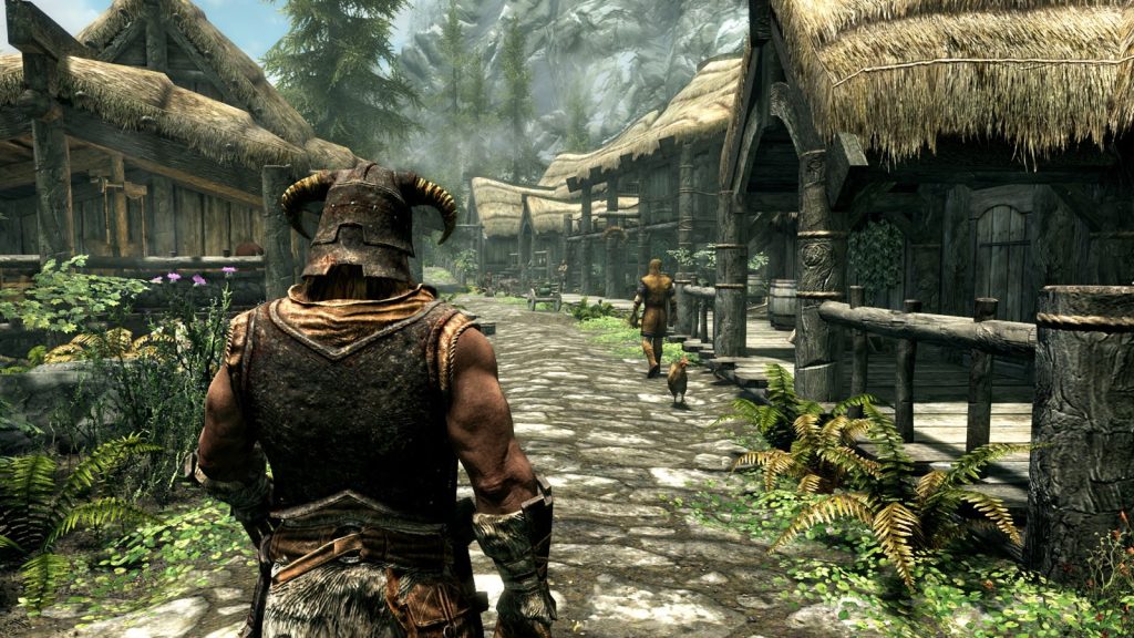 A character in a horned helmet walks down a village street lined with wooden houses in Skyrim