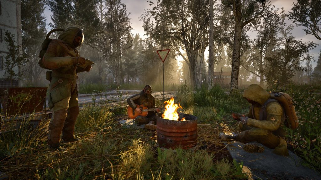 Three stalkers in protective suits rest around a fire in a barrel, one playing a guitar