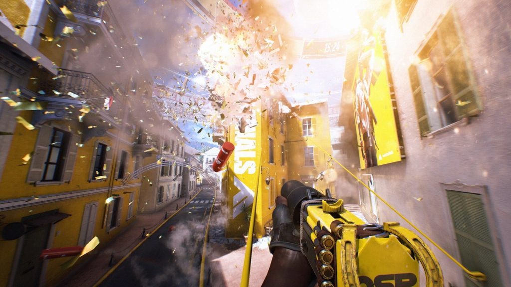 First-person view of a player holding a yellow weapon as an explosion blows debris across a street of yellow buildings