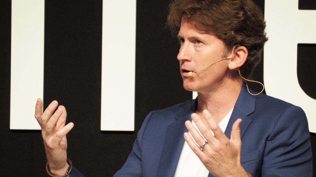 Todd Howard gestures while speaking on stage, wearing a headset microphone