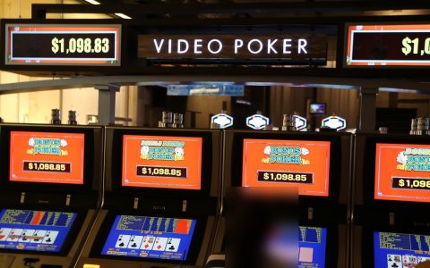 A row of video poker machines with orange screens under a lit Video Poker sign